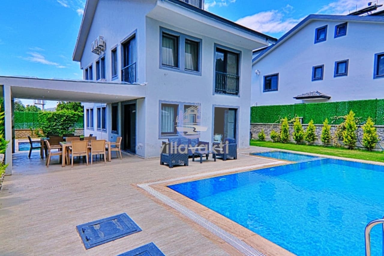 Bahçesinde özel havuz ve yemek masası bulunan iki katlı beyaz villa.