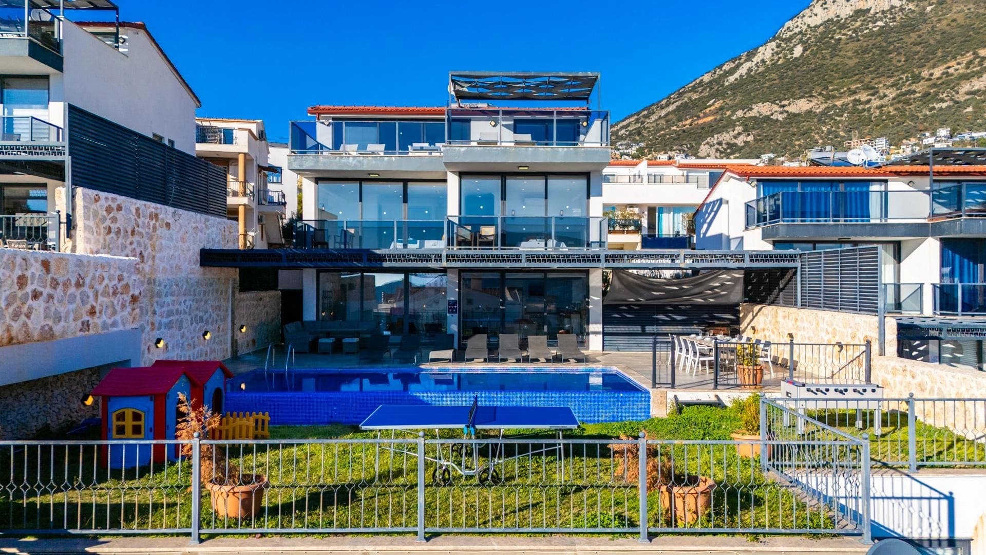 Önünde havuz, masa tenisi ve çocuk oyun evi bulunan üç katlı modern villa.