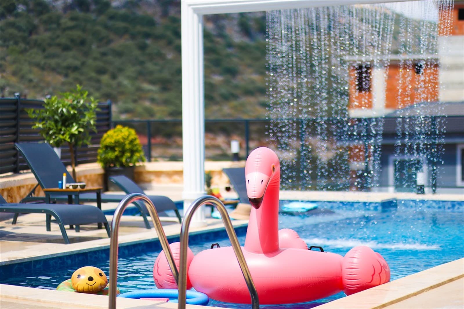 Açık havuzda pembe flamingo deniz yatağı ve şezlonglar bulunan havuz terası.