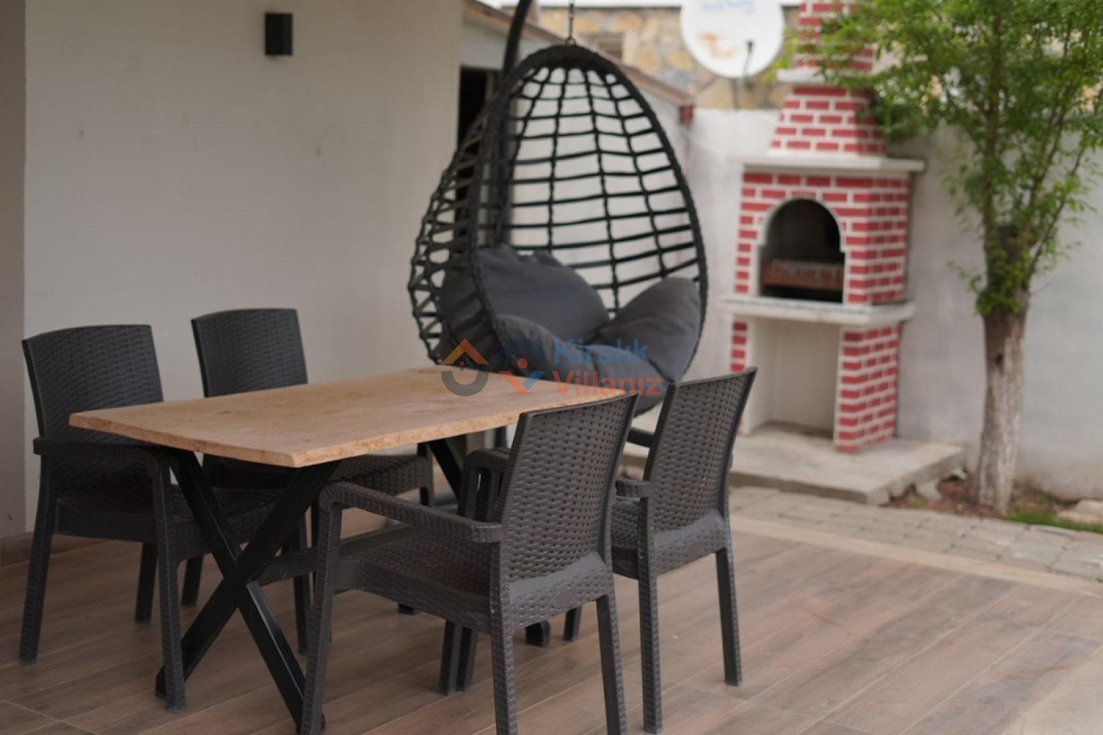 Bahçede ahşap yemek masası, sandalyeler, salıncak ve tuğla barbekü alanı.