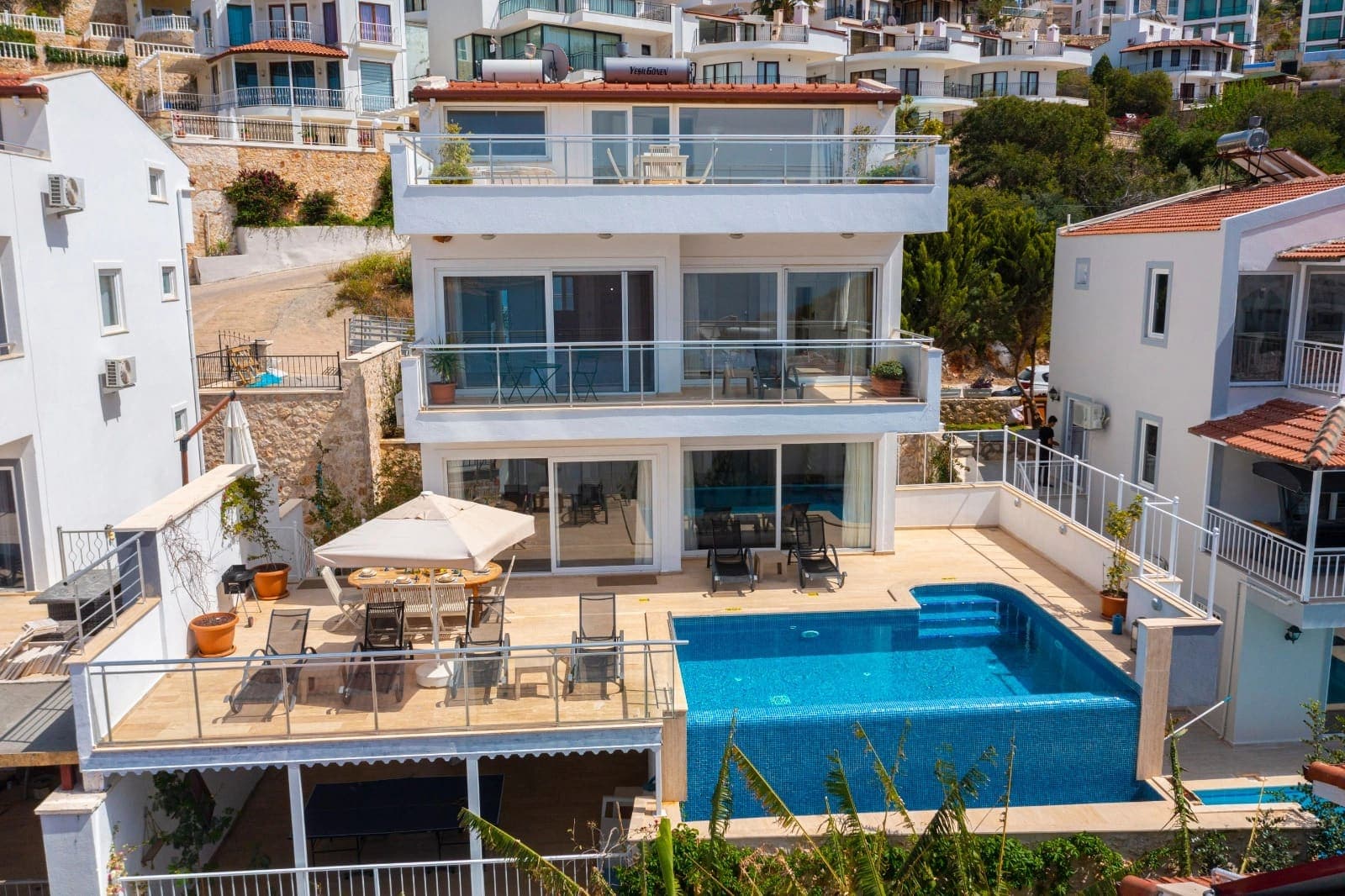 Önünde yüzme havuzu ve şezlonglar bulunan beyaz katlı villa