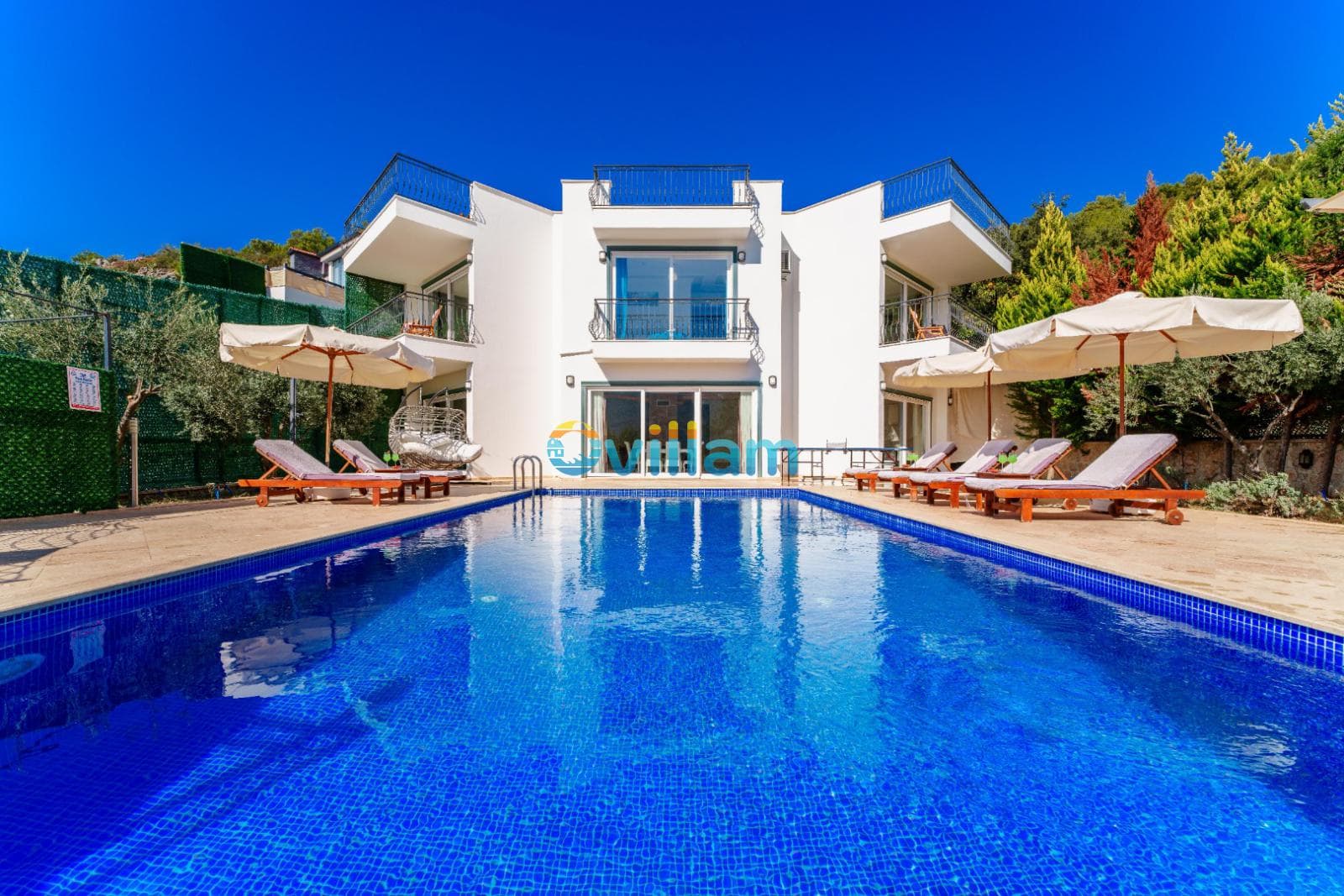 Geniş yüzme havuzu ve arkasında yer alan beyaz modern villa binası.