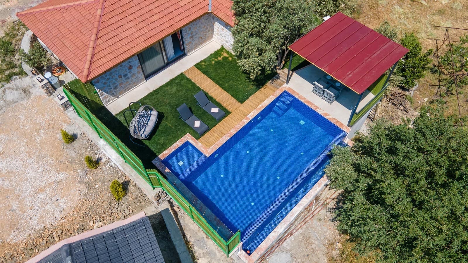 Havuz kenarında şezlonglar, salıncak ve çardak bulunan villa bahçesinin havadan görünümü.