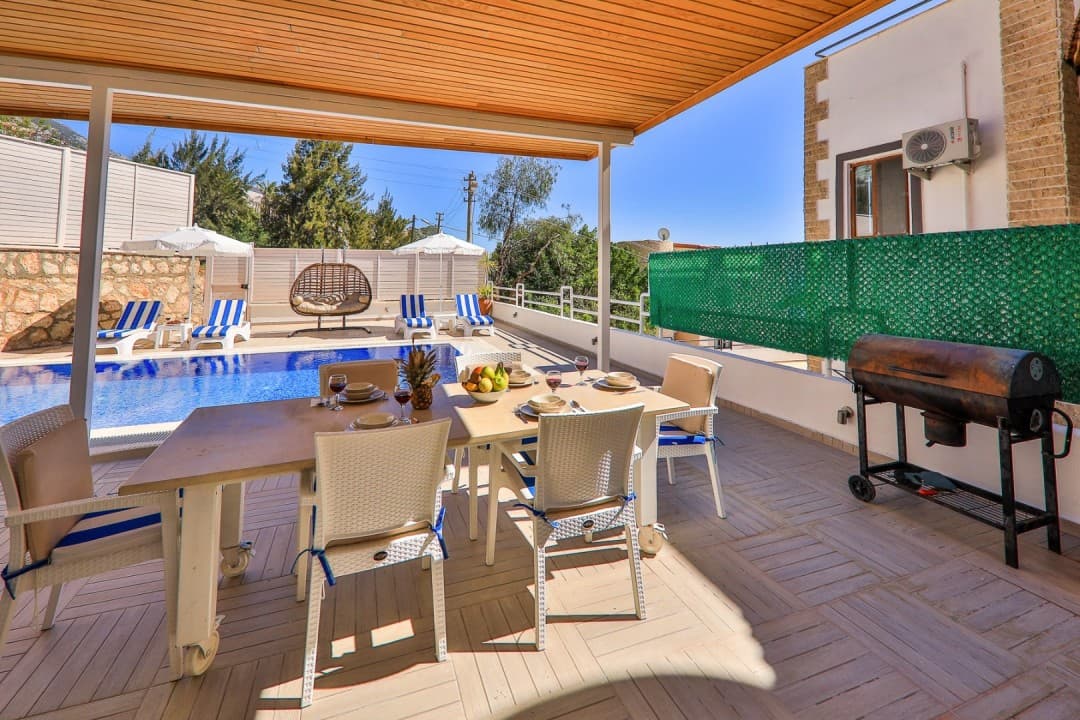 Gölge pergola altında yemek masası ve arka planda açık havuz.