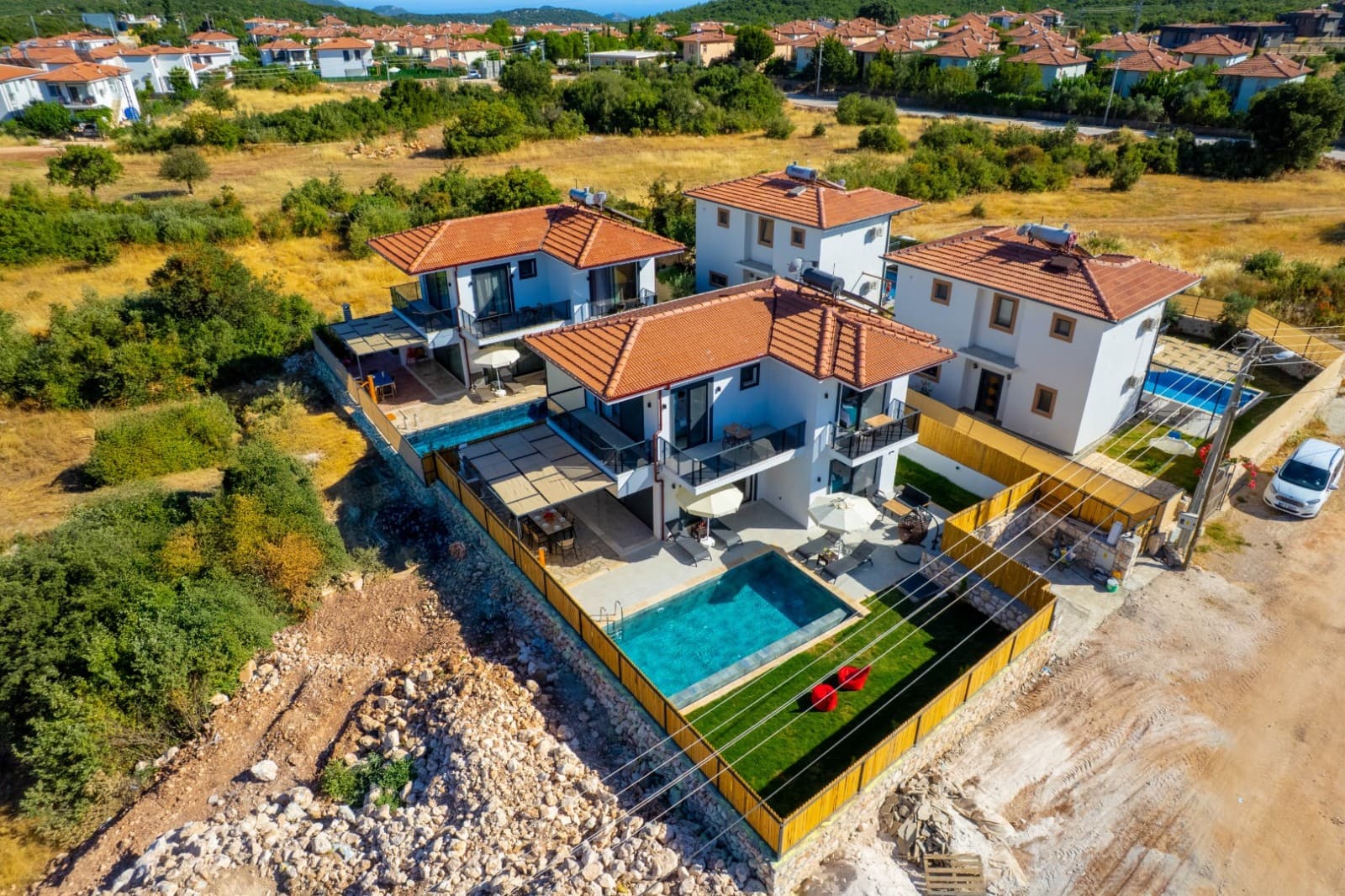 Havuzlu ve kiremit çatılı beyaz villaların havadan görünümü.