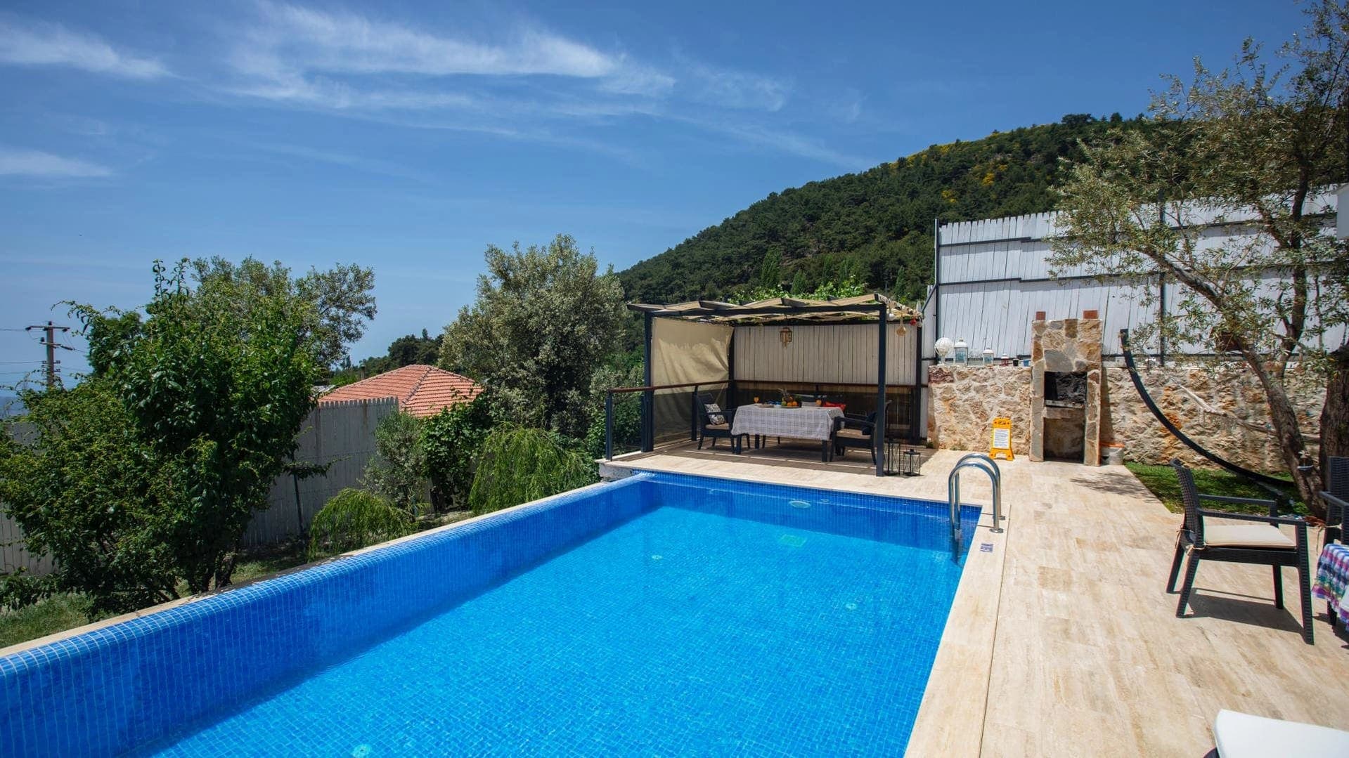 Dağ manzaralı terasta özel yüzme havuzu, gölgelikli yemek alanı ve taş barbekü.