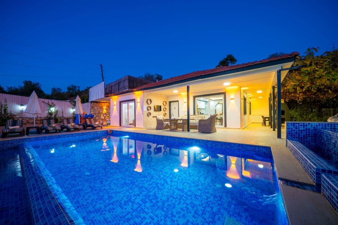 Gece aydınlatmalı havuzu, şezlongları ve verandasında oturma grubu bulunan tek katlı müstakil villa.