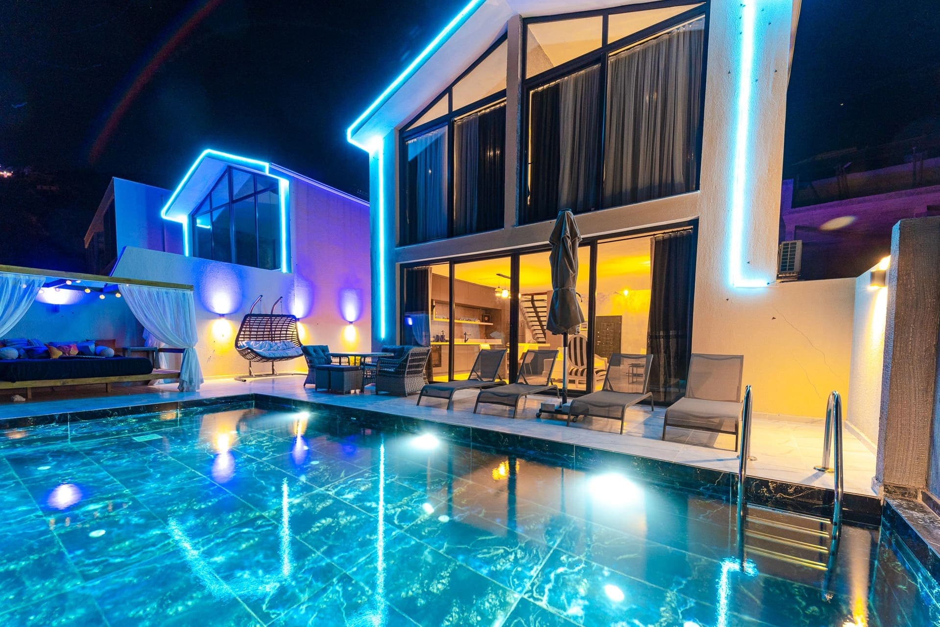 Mavi LED ışıklarla aydınlatılmış iki katlı modern villa, gece vakti ışıklandırılmış yüzme havuzu.