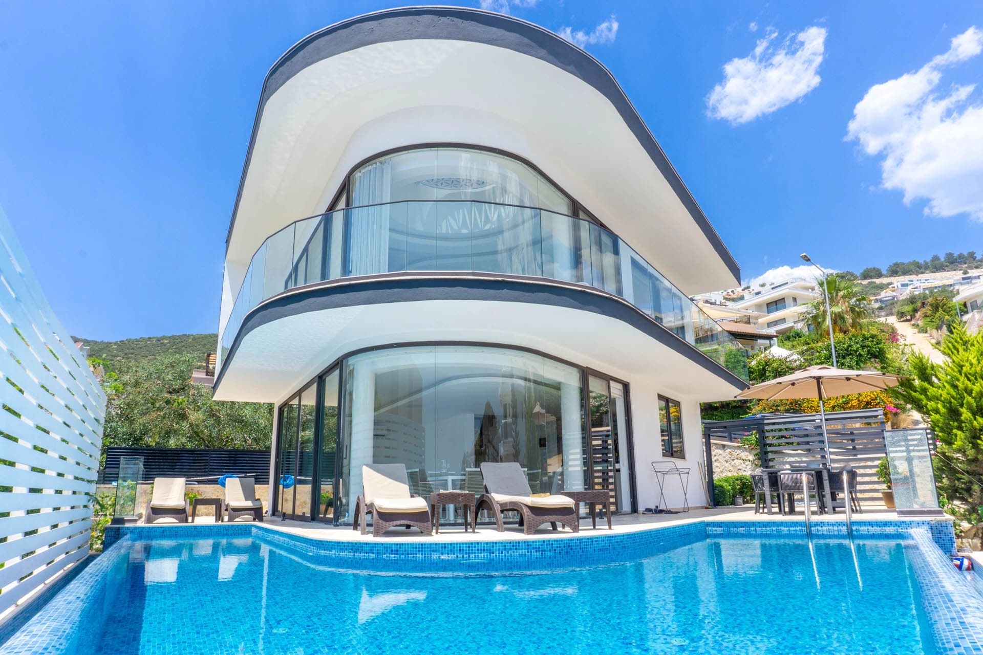 Kavisli mimariye sahip iki katlı beyaz villa, önünde özel yüzme havuzu ve şezlonglar.
