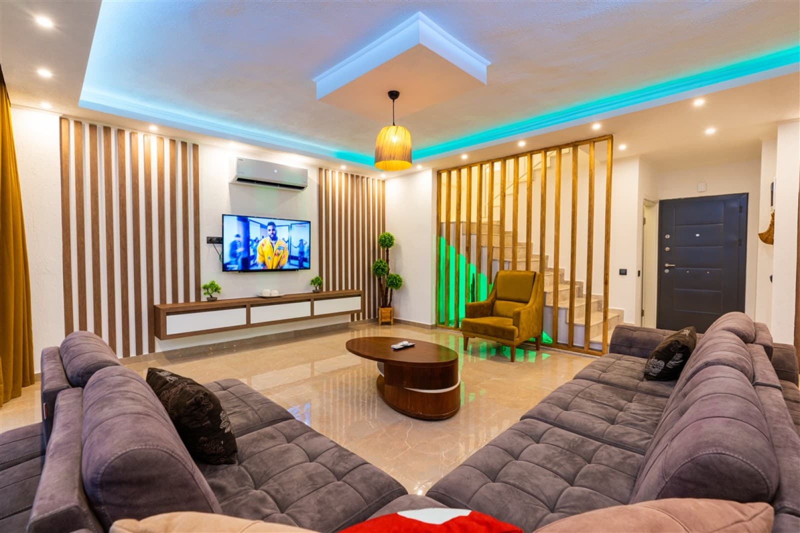 Modern salon, gri köşe koltuk, ahşap detaylı TV ünitesi ve merdiven.