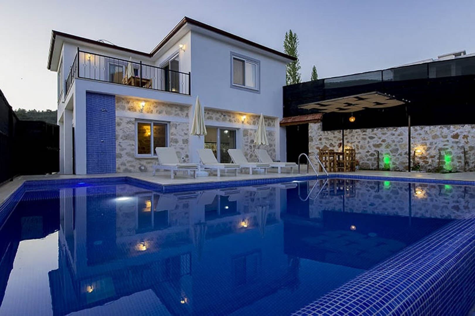 Önünde mavi havuz ve şezlonglar olan beyaz villa ve bahçesi.