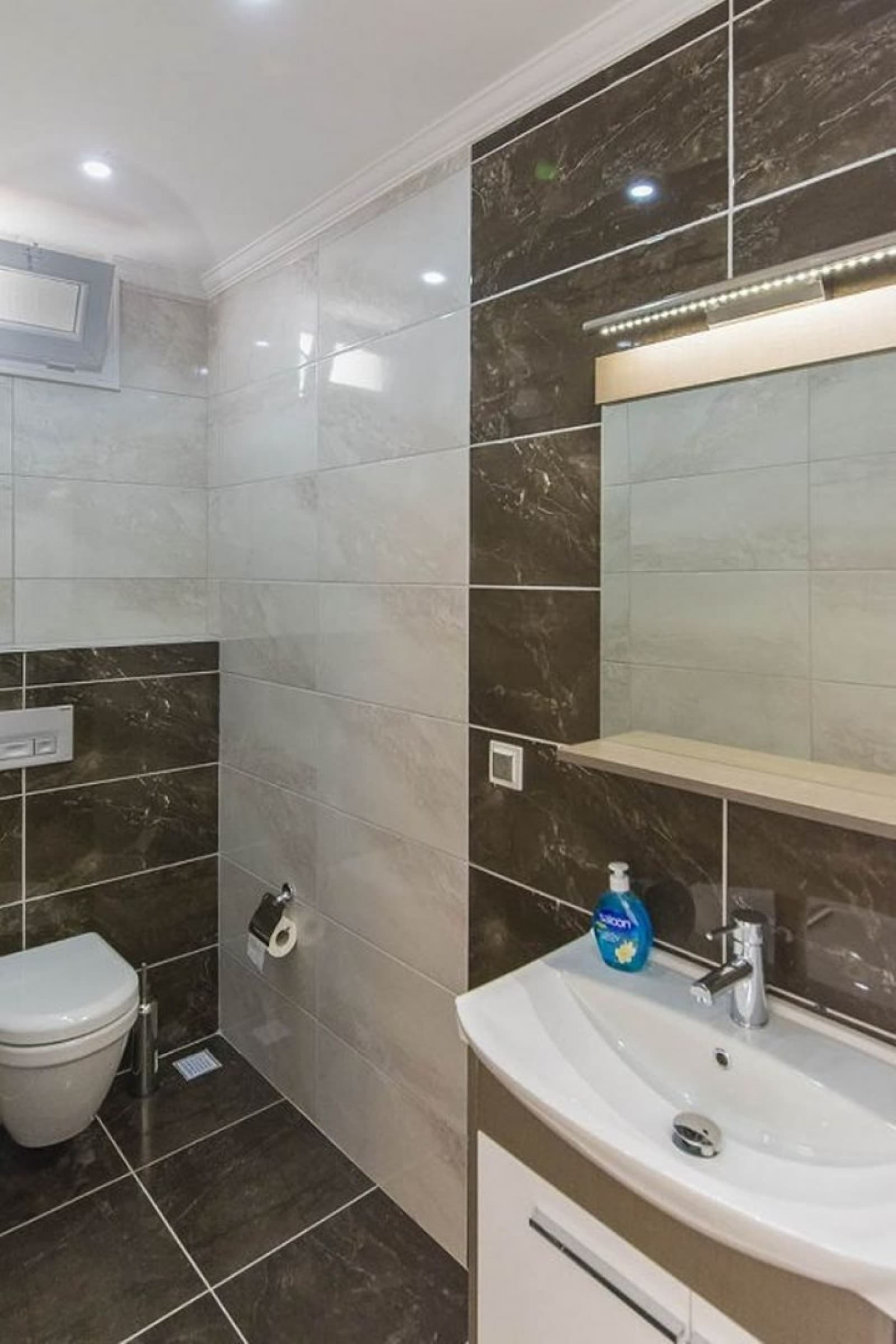Kahverengi ve krem seramik kaplı banyoda lavabo, ayna ve klozet.