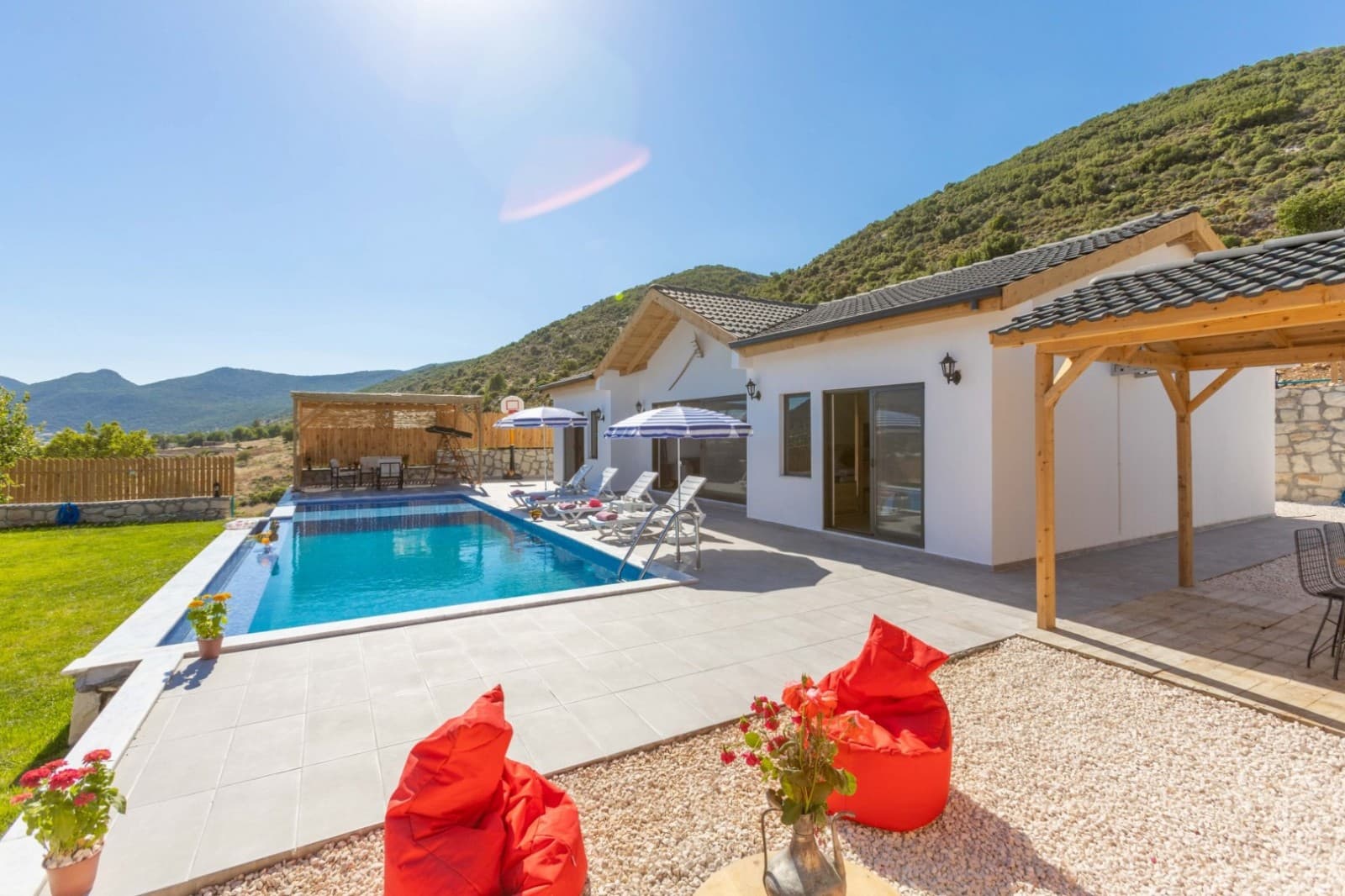 Beyaz villanın önünde yüzme havuzu, şezlonglar ve dağ manzarası.