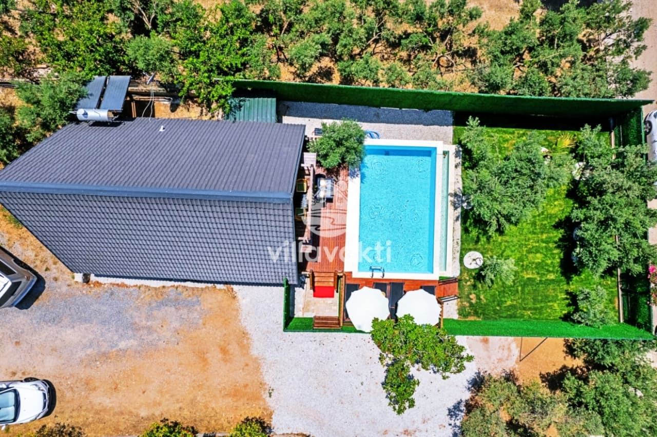 Kuş bakışı görünümde siyah çatılı ahşap bungalov, özel yüzme havuzu ve yeşil bahçe.