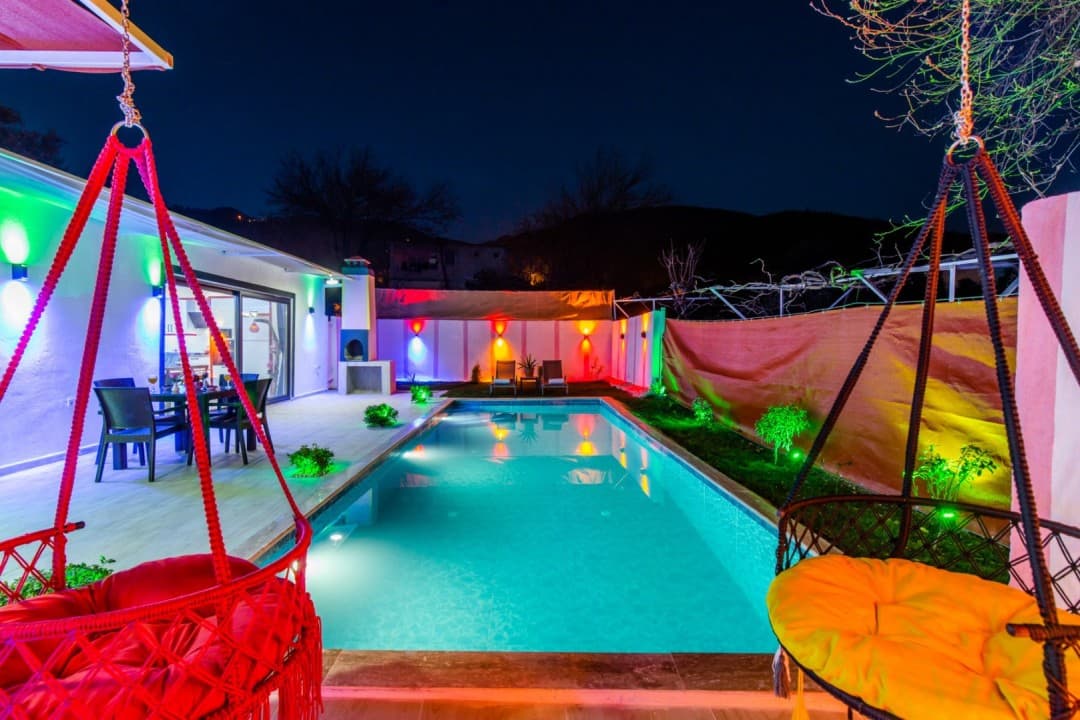 Gecenin karanlığında renkli ışıklandırmalı havuz ve bahçesinde asılı salıncaklar.