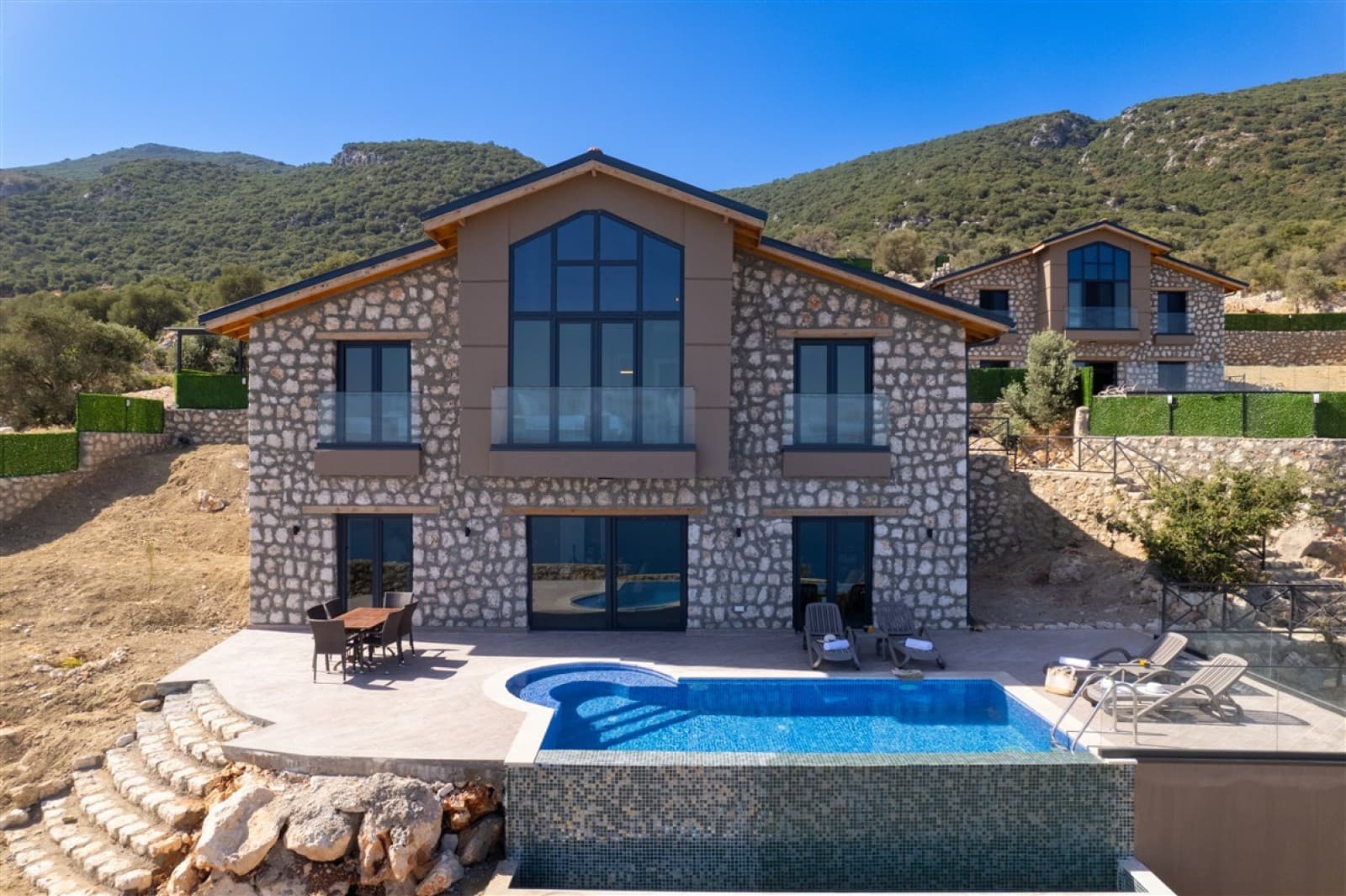 Dağ manzaralı, taş kaplamalı dış cephesi ve önünde havuzu olan iki katlı villa.
