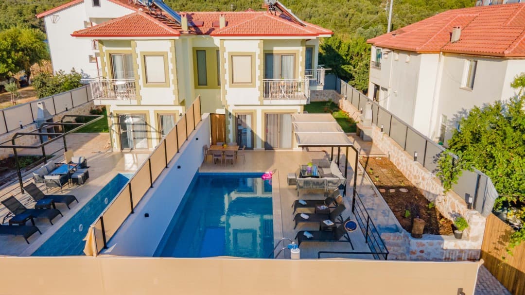 Çift katlı villa, müstakil havuz, şezlonglar, oturma grubu ve yemek masası.