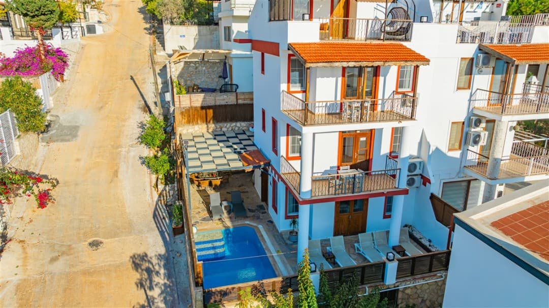 Üç katlı beyaz villanın önünde özel havuz, şezlonglar ve gölgelikli oturma alanı bulunuyor.