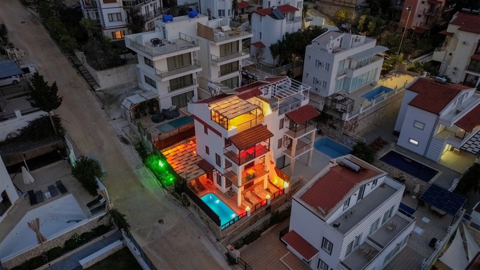 Gece çekiminde aydınlatılmış beyaz dış cepheye sahip çok katlı villa havuzla çevrili.