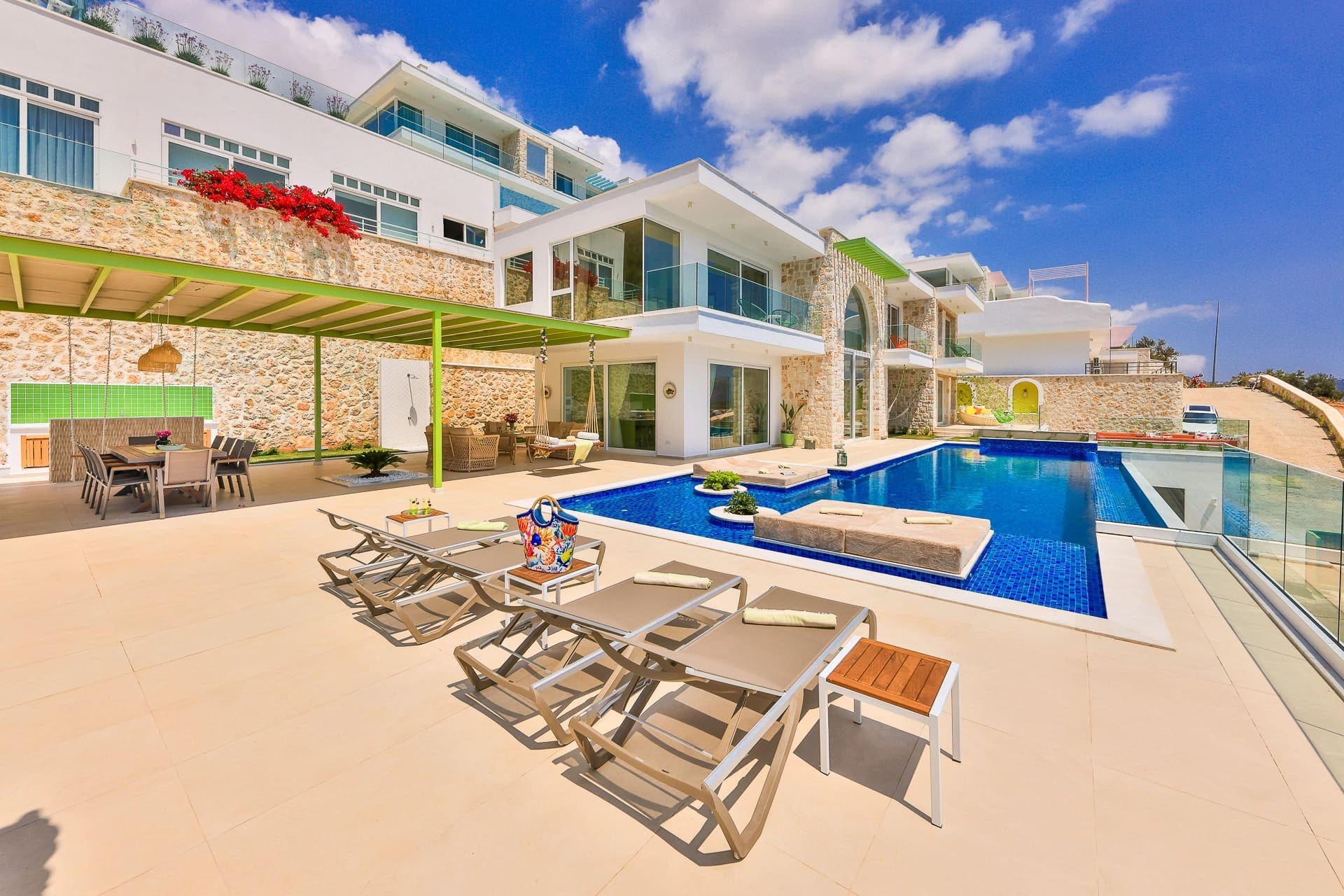 Güneşlenme şezlongları, yemek alanı ve geniş yüzme havuzu ile modern lüks villa dış cephesi.