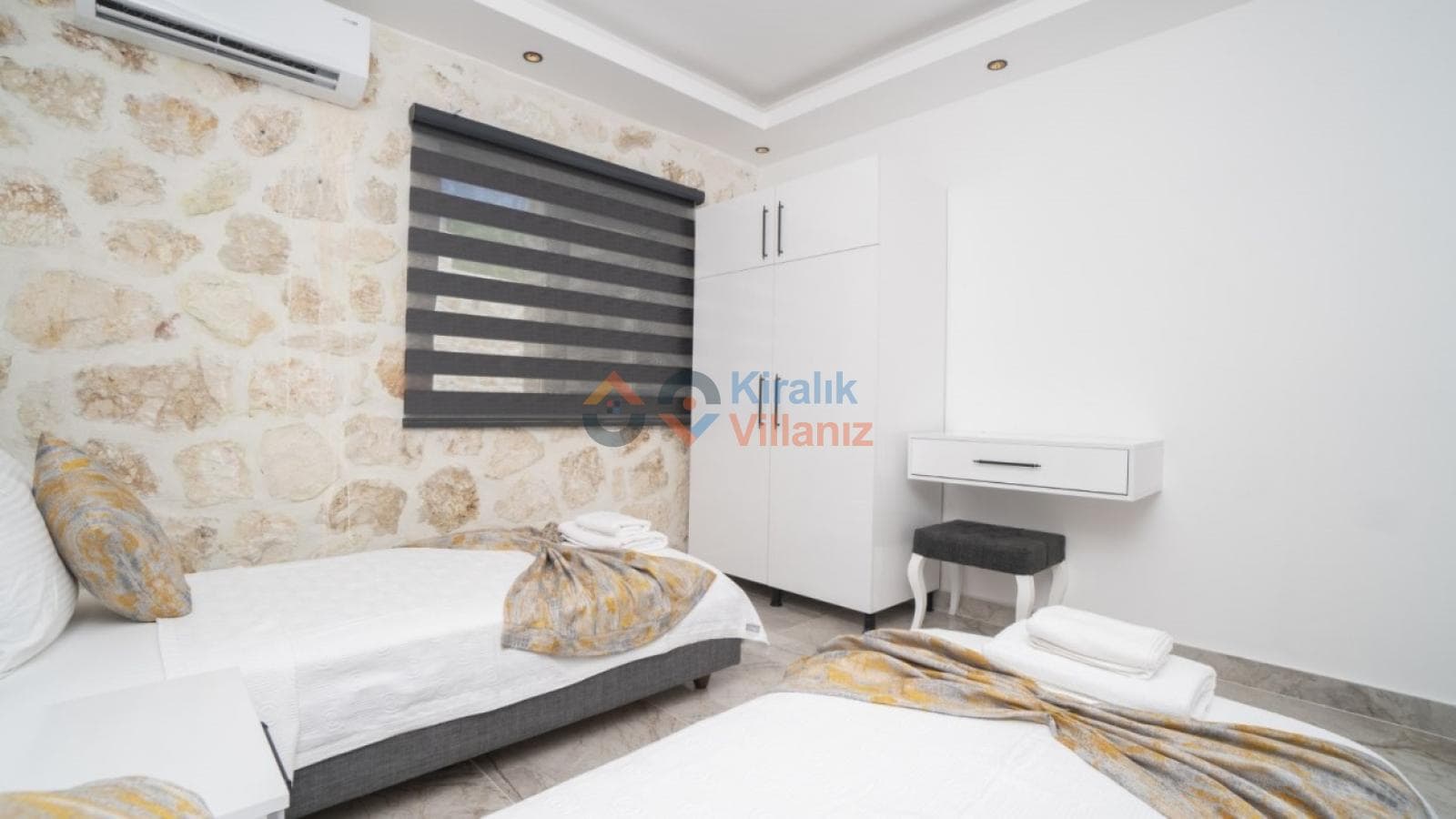Taş duvar kaplamalı yatak odasında iki adet tek kişilik yatak, gardırop ve makyaj masası.