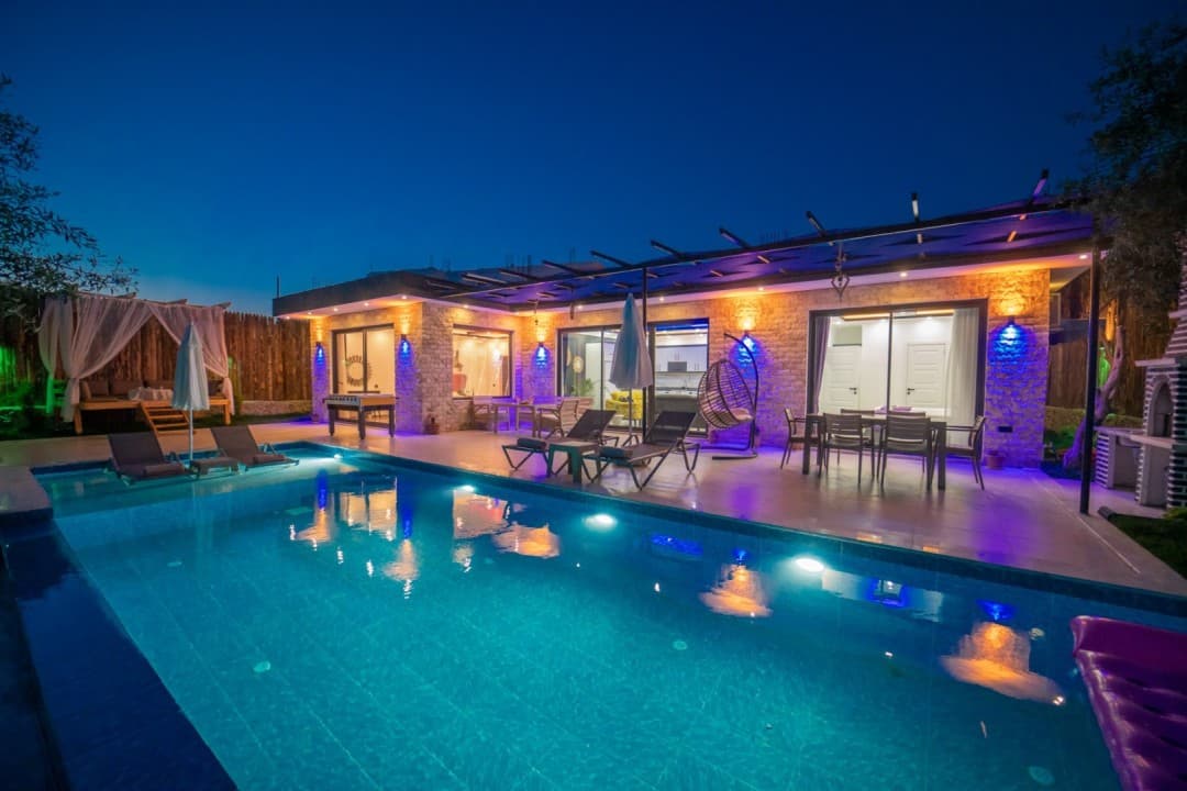 Akşam saatlerinde havuzu ve ışıklandırılmış verandası görünen villa dış cephesi.