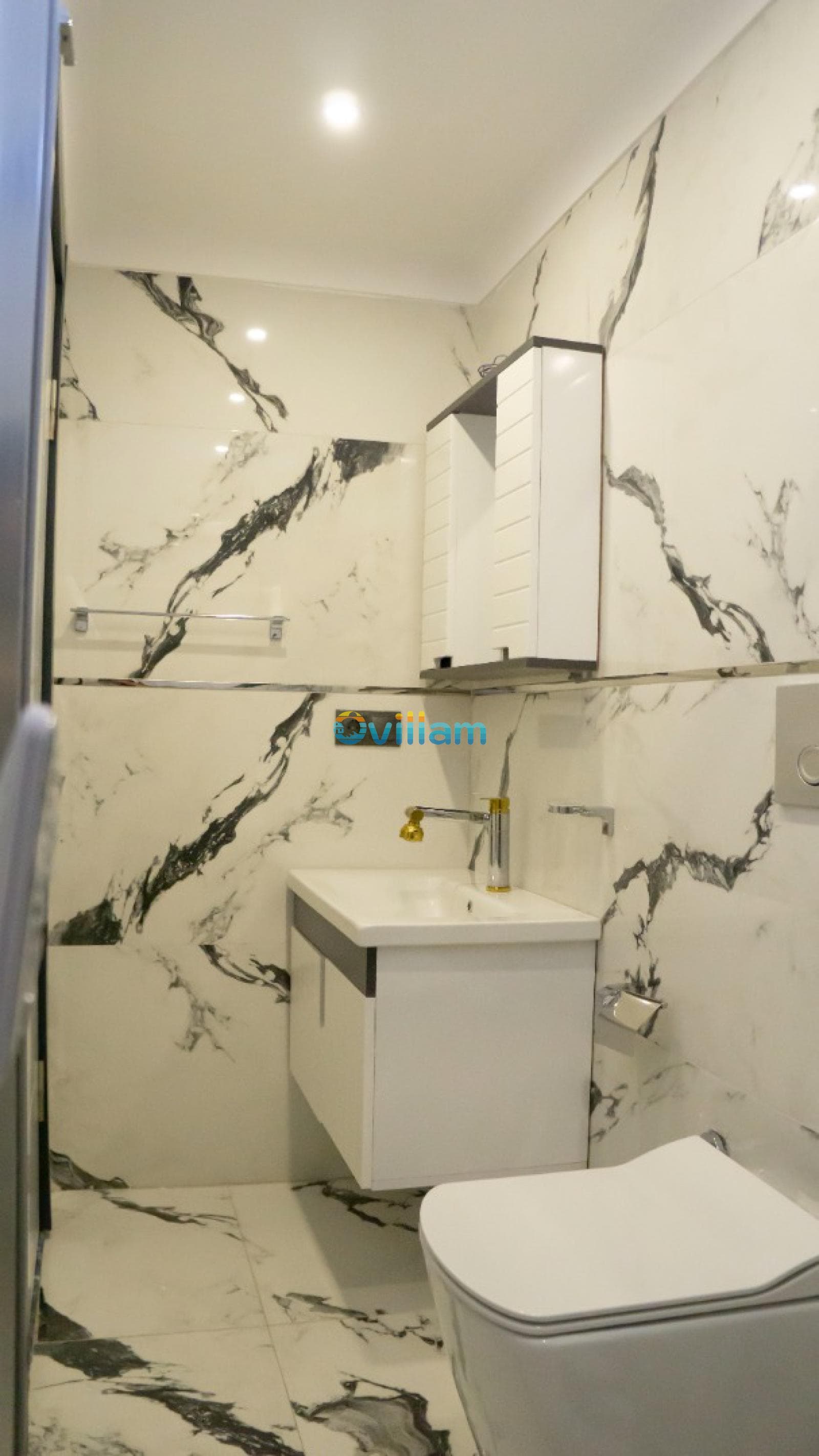 Mermer desenli fayanslarla kaplı banyoda beyaz lavabo dolabı, ayna ve klozet.