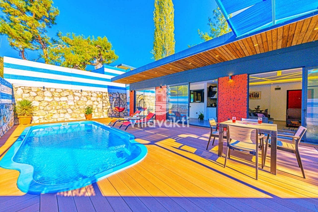 Ahşap zeminli verandada özel yüzme havuzu, yemek masası takımı ve modern villa cephesi.