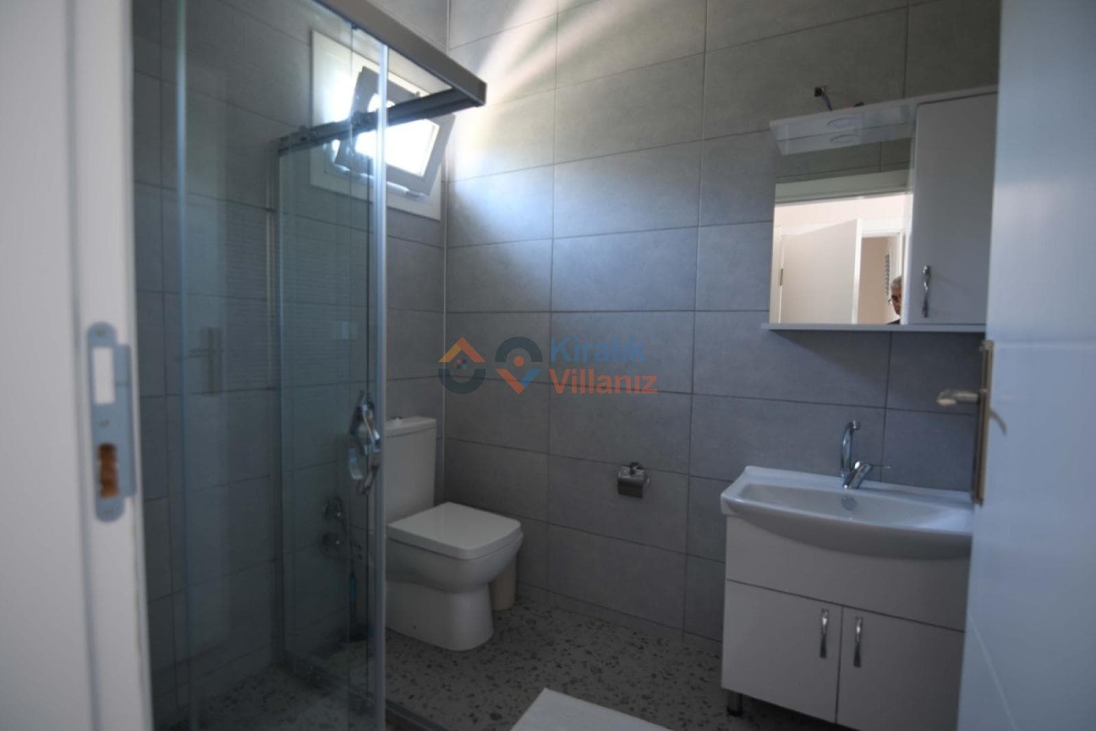 Gri seramik kaplı banyoda duşakabin, tuvalet ve aynalı lavabo yer alıyor.