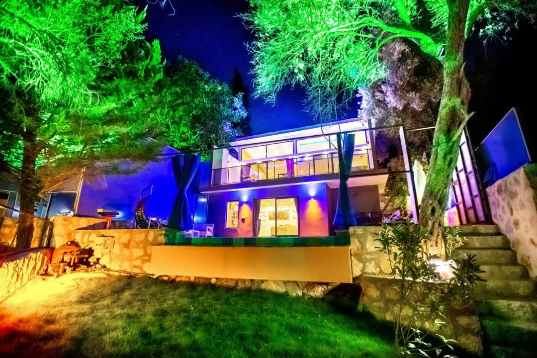 Yeşil ve mavi ışıklarla aydınlatılmış, iki katlı villanın gece görünümü.