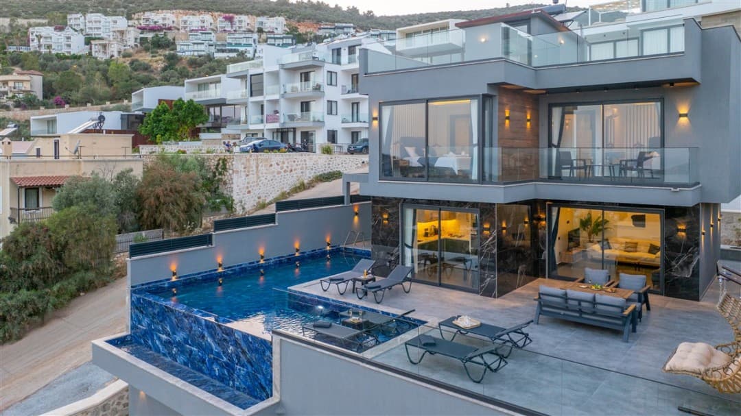 Gri modern villanın önünde havuz, şezlonglar ve oturma grubu bulunuyor.