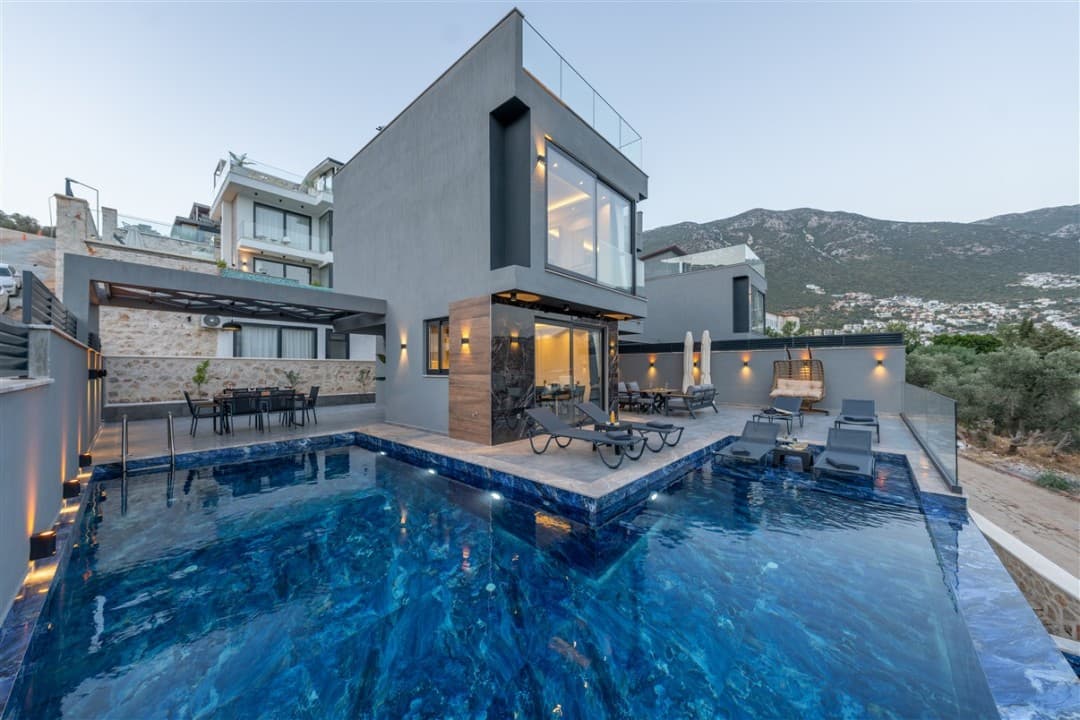 Önünde mavi havuz ve şezlonglar olan gri dış cepheli modern villa.