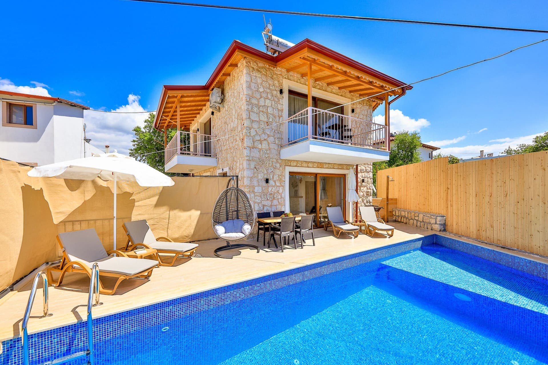 Taş kaplı dış cephesi ve havuz başında şezlongları olan villa.