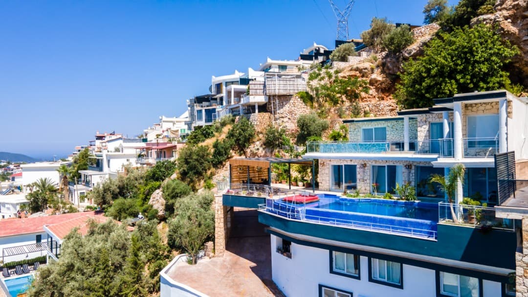 Yamaç üzerine kurulu, sonsuzluk havuzlu ve geniş teraslı beyaz dış cepheli villa.