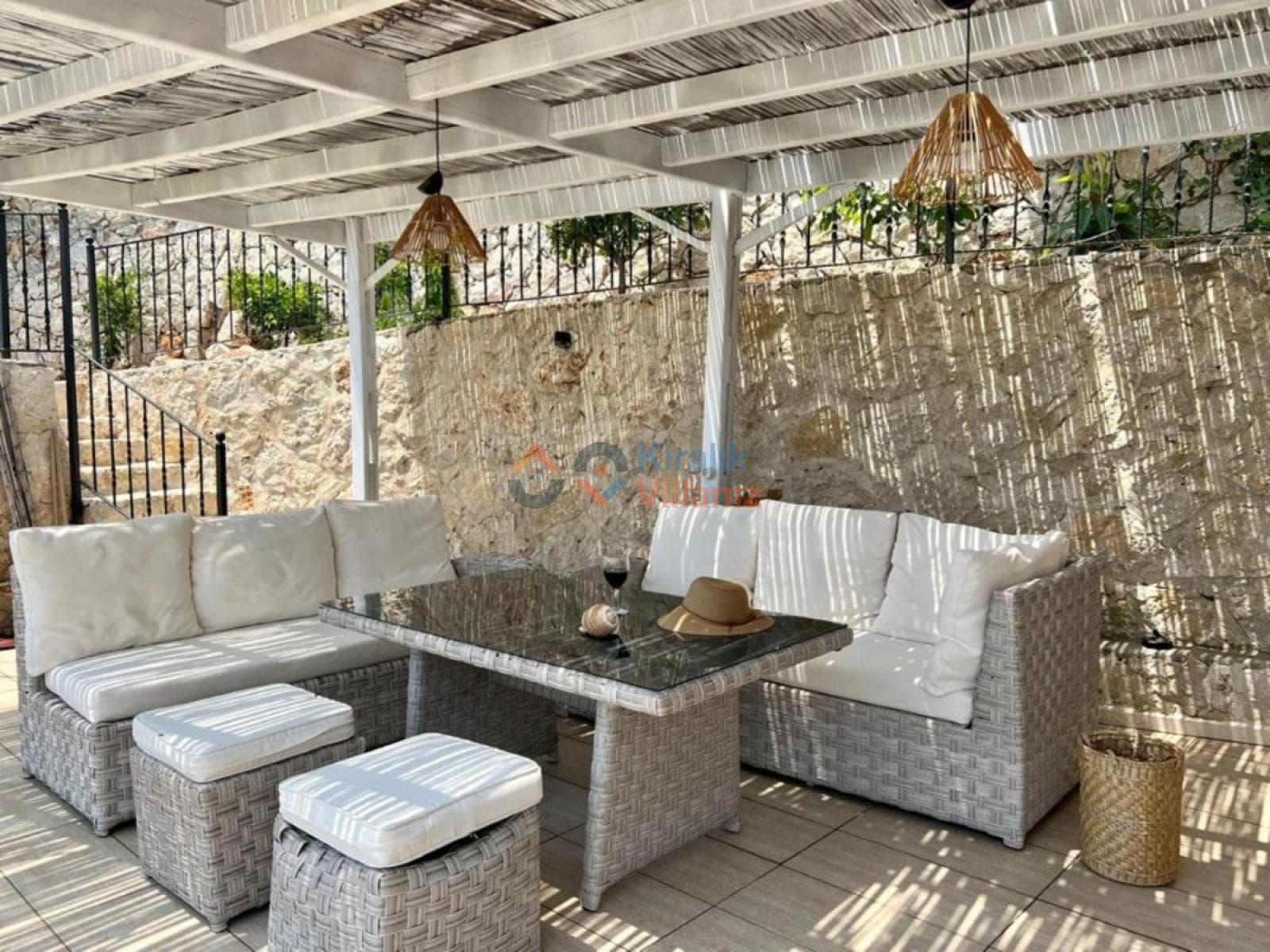 Pergola altında beyaz minderli oturma grubu ve sehpa.