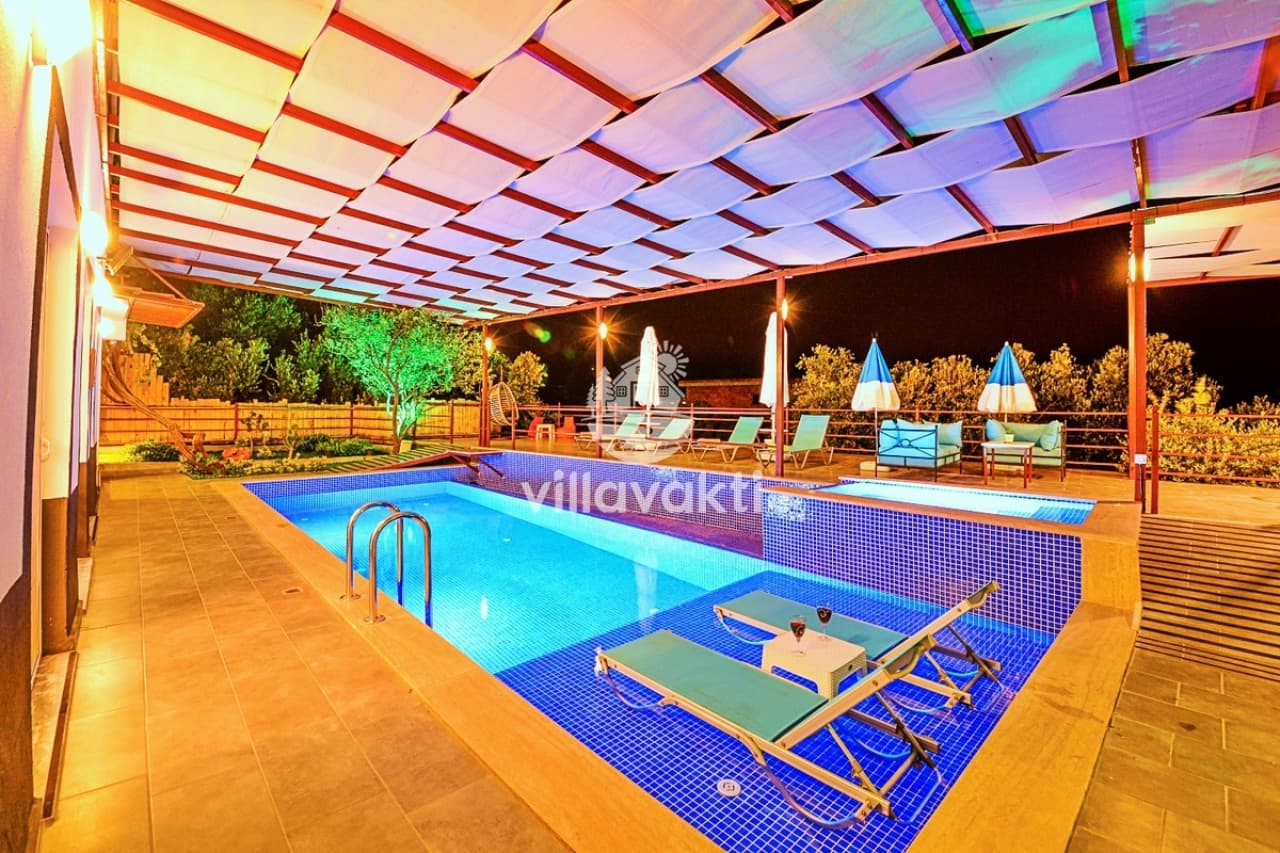 Güneşlikli pergola altında mavi mozaikli açık havuz ve şezlonglar.
