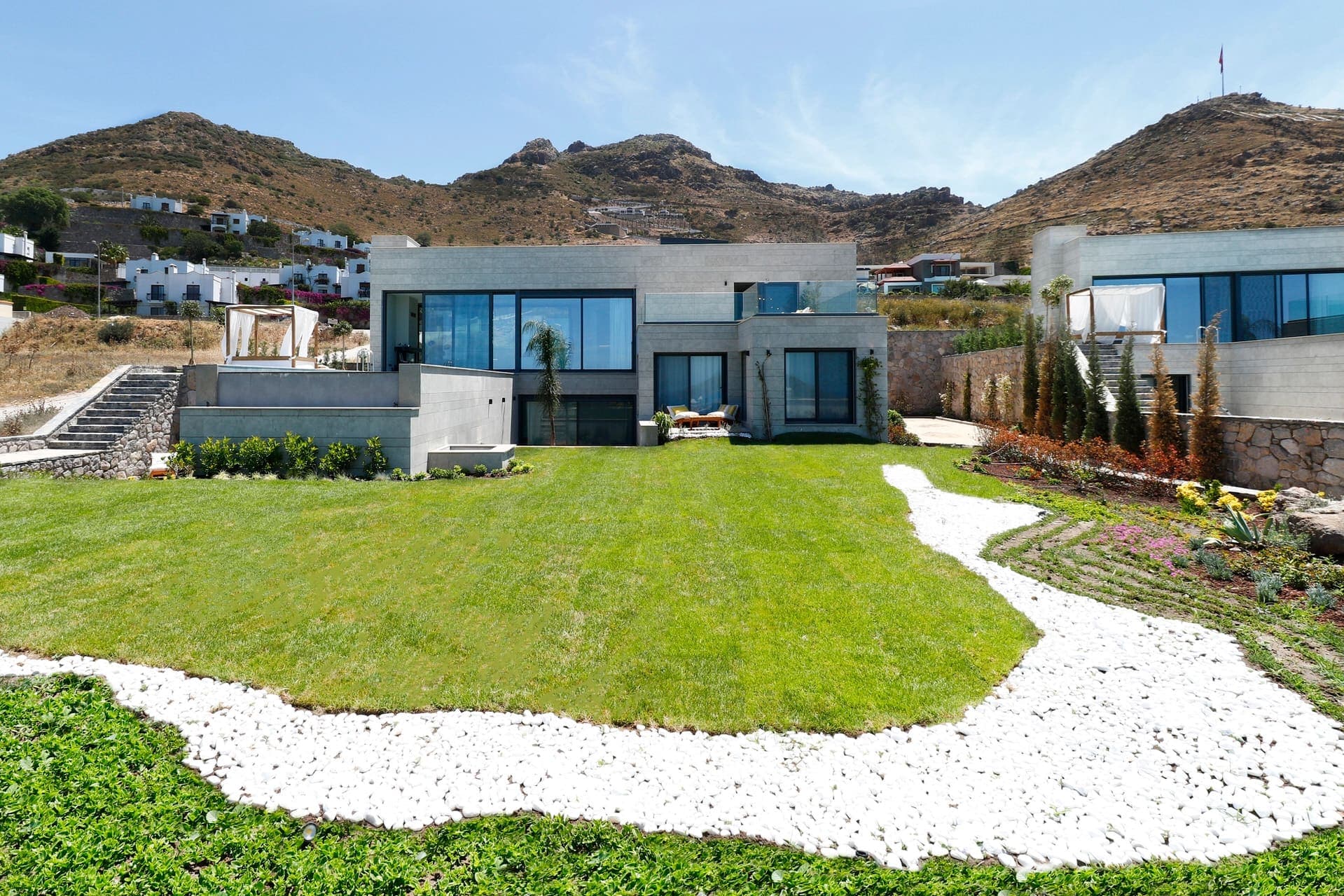 Geniş çim bahçeye bakan modern dış cepheli villa ve dağ manzarası.