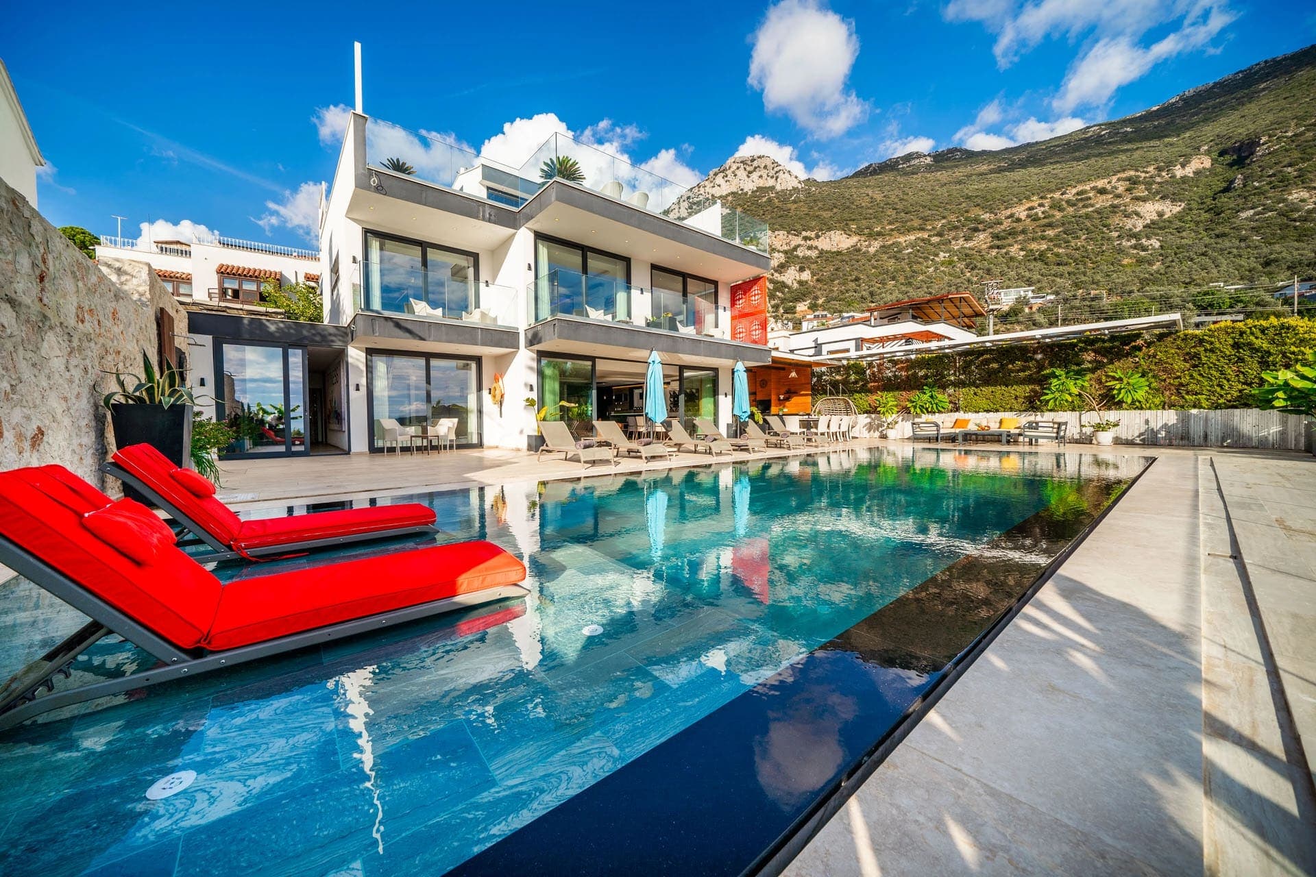 Dağ manzaralı havuz kenarında kırmızı şezlonglar bulunan modern villa