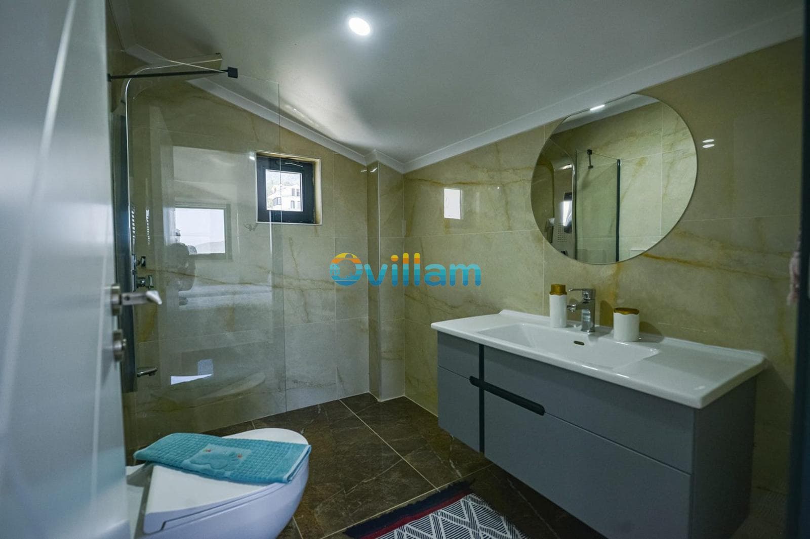 Bej seramik kaplı banyoda duşakabin, yuvarlak ayna ve lavabo bulunuyor.