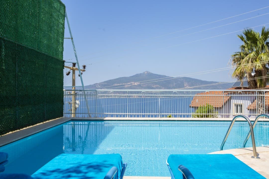 Mavi havuz önünde deniz ve dağ manzaralı balkon.