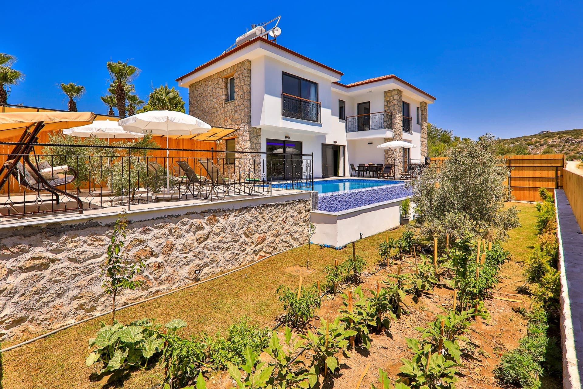 Bahçesinde ekili sebzeler ve havuzu bulunan beyaz taş villa.