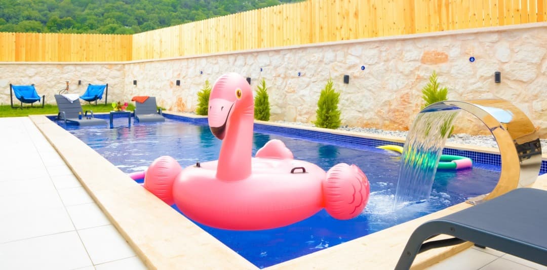 Taş duvarlarla çevrili havuzda pembe flamingo deniz yatağı, şelale sistemi ve şezlonglar bulunuyor.