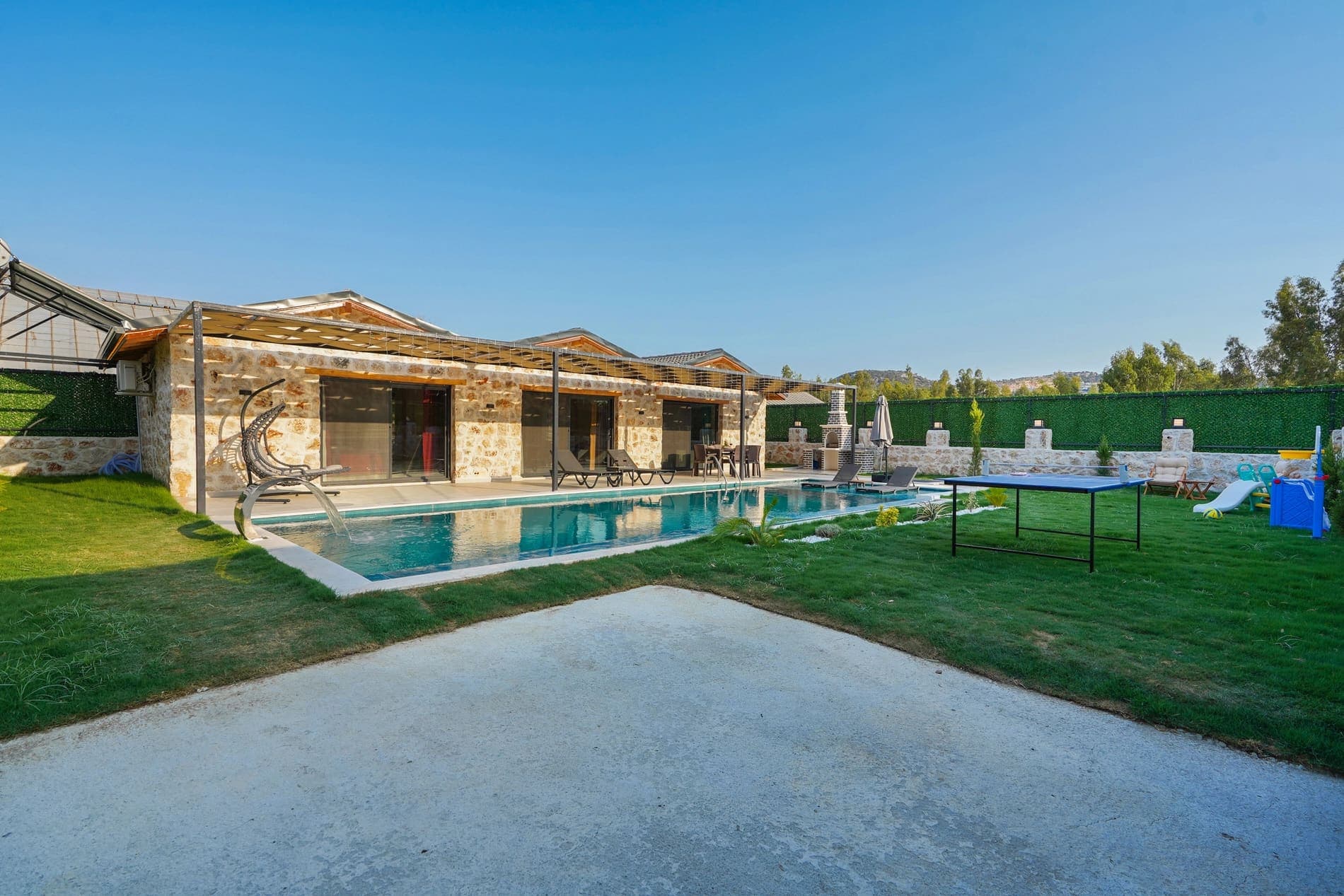 Önünde yüzme havuzu ve çimenlik bahçe bulunan taş cepheli villa.