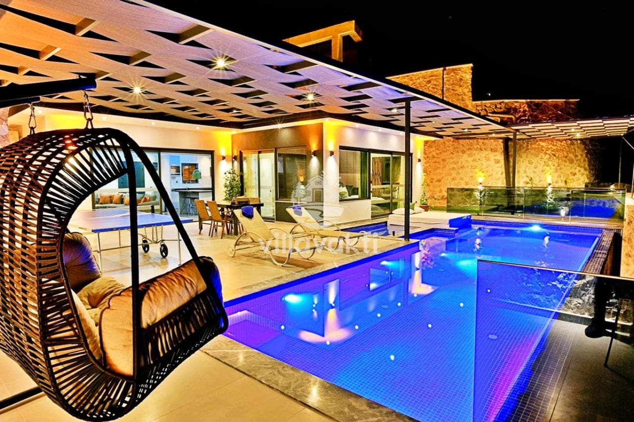 Akşam aydınlatmalı havuz başı ve salıncak bulunan villa dış cephesi.
