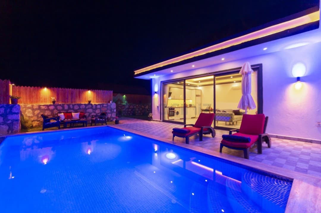 Gece vaktinde havuz başında şezlonglar ve aydınlatılmış villa cephesi.