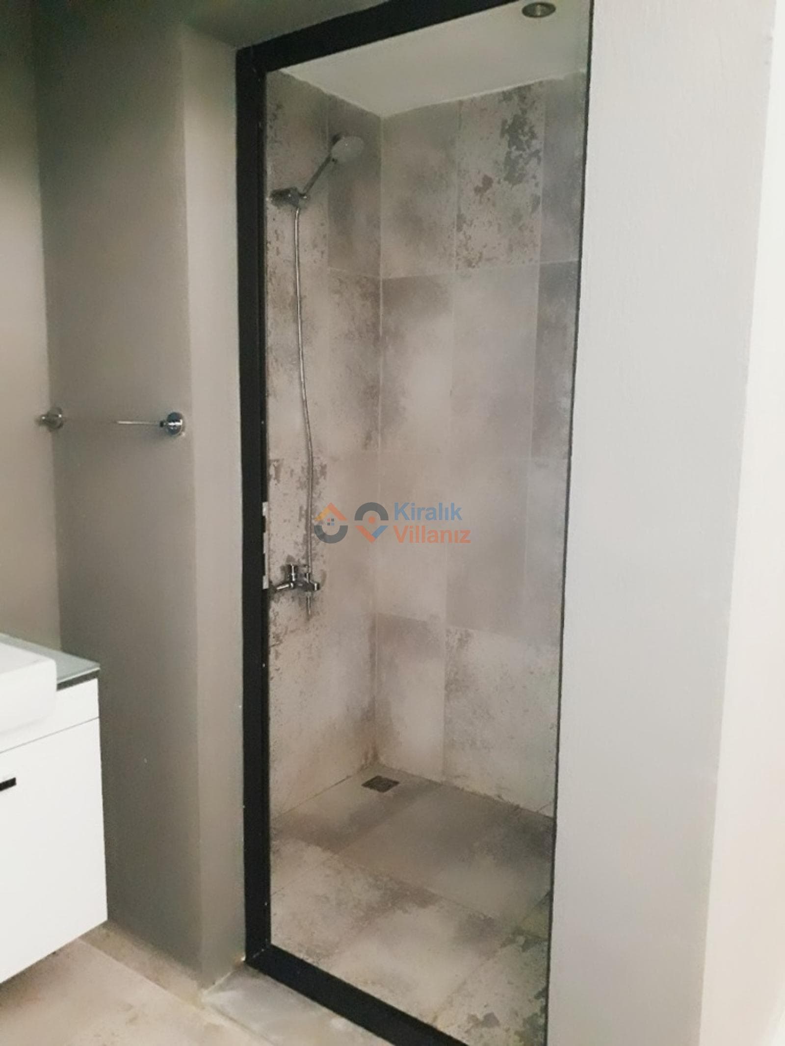Siyah çerçeveli cam duş kabini ve gri tonlarda seramik banyo.