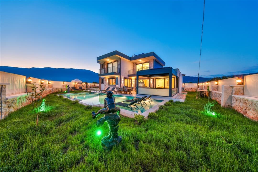 Akşam vaktinde bahçesinde heykeller, yüzme havuzu ve şezlonglar bulunan iki katlı modern villa.