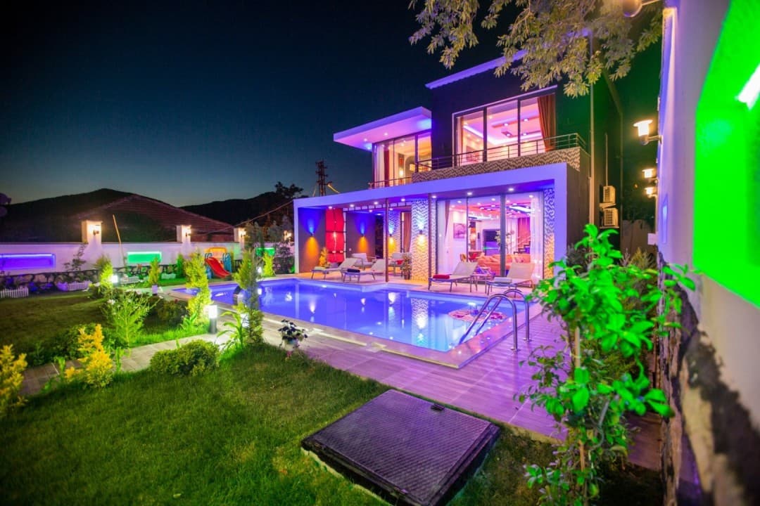 Gece aydınlatmalı, havuzlu ve bahçeli iki katlı modern villa dış görünümü.