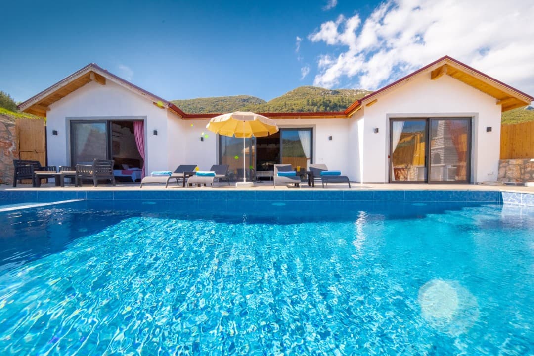 Önünde havuz, şezlonglar ve sarı şemsiye bulunan beyaz dış cepheli tek katlı villa.