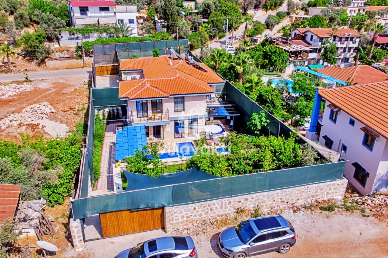 Ağaçlarla çevrili bahçesi ve havuzu olan iki katlı villanın havadan görünümü.